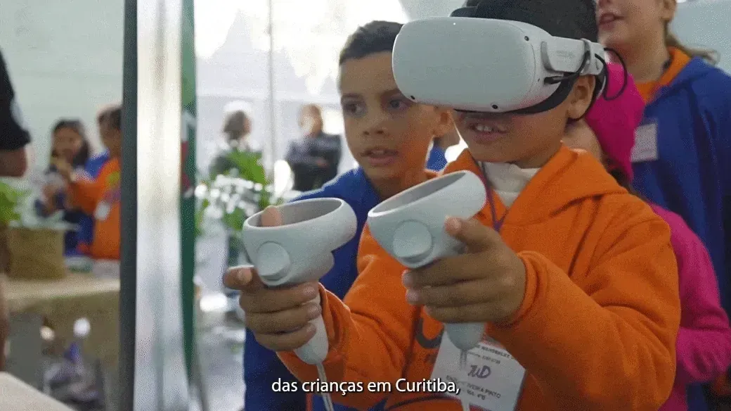 mK VR (ativação em realidade virtual/metaverso): crianças usando óculos de realidade virtual e controles em evento em Curitiba, vestindo agasalhos laranja e azul
